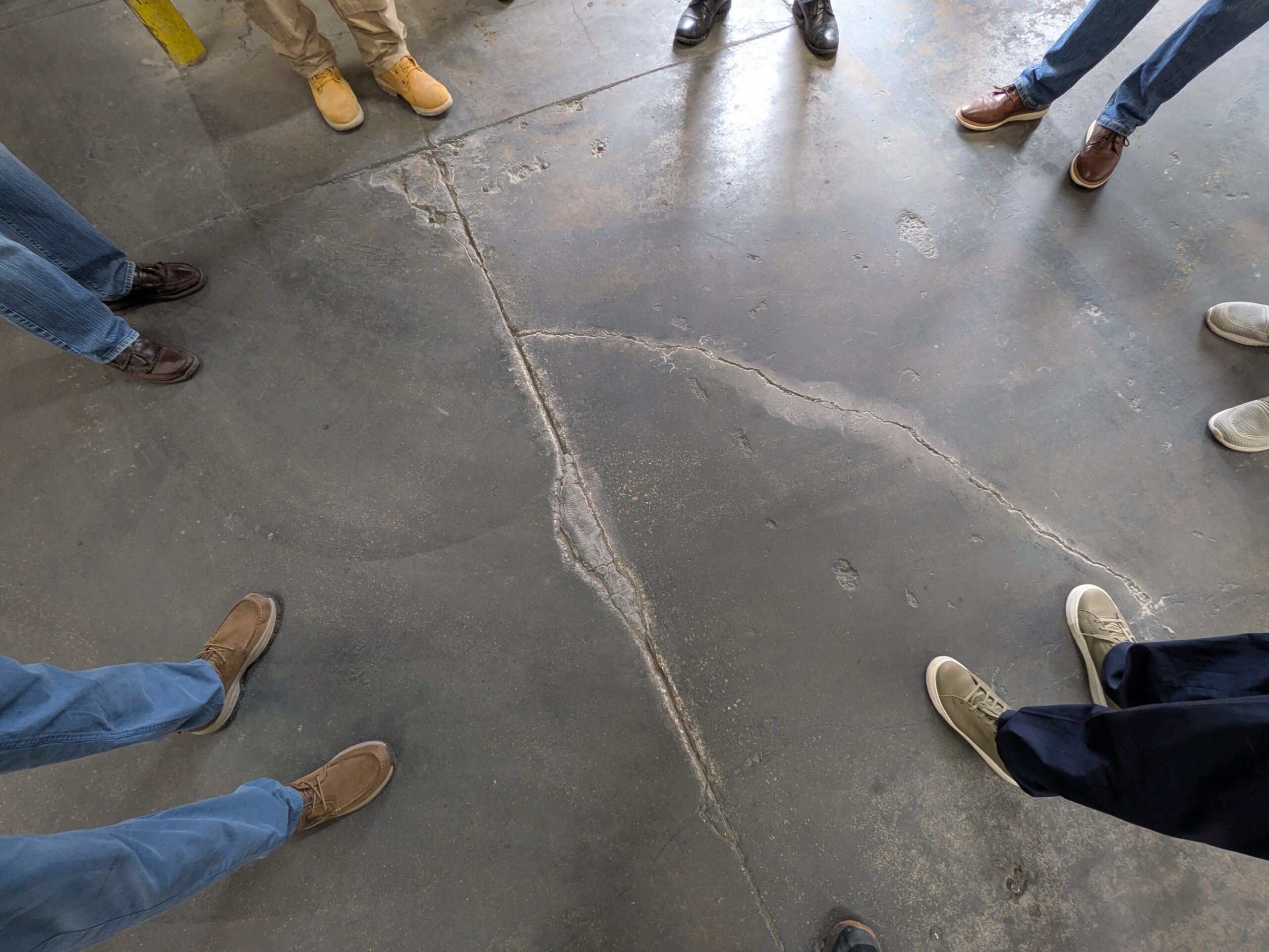 Overhead photo of concrete warehouse with people looking at floor crack before being repaired with FasTrac Crackweld Pro.